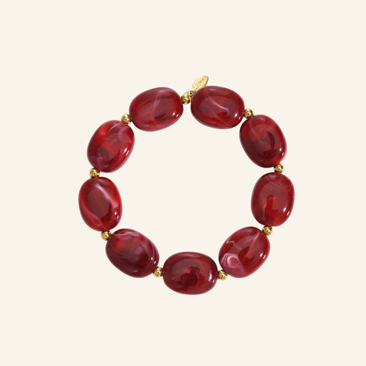 Ovale kralenarmband met goud – karmijnrood vrijstaand op beige