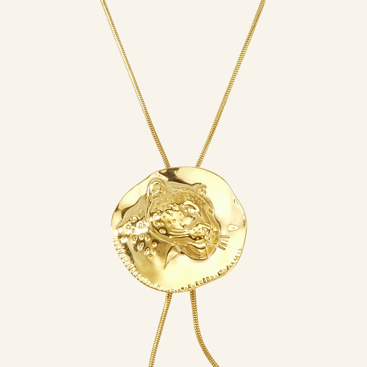 Luipaard munt ketting goud – detail van de hanger op beige