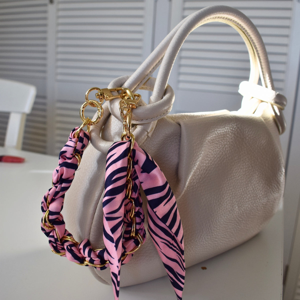 Sjaal bag charm roze met gouden kettingen aan witte tas