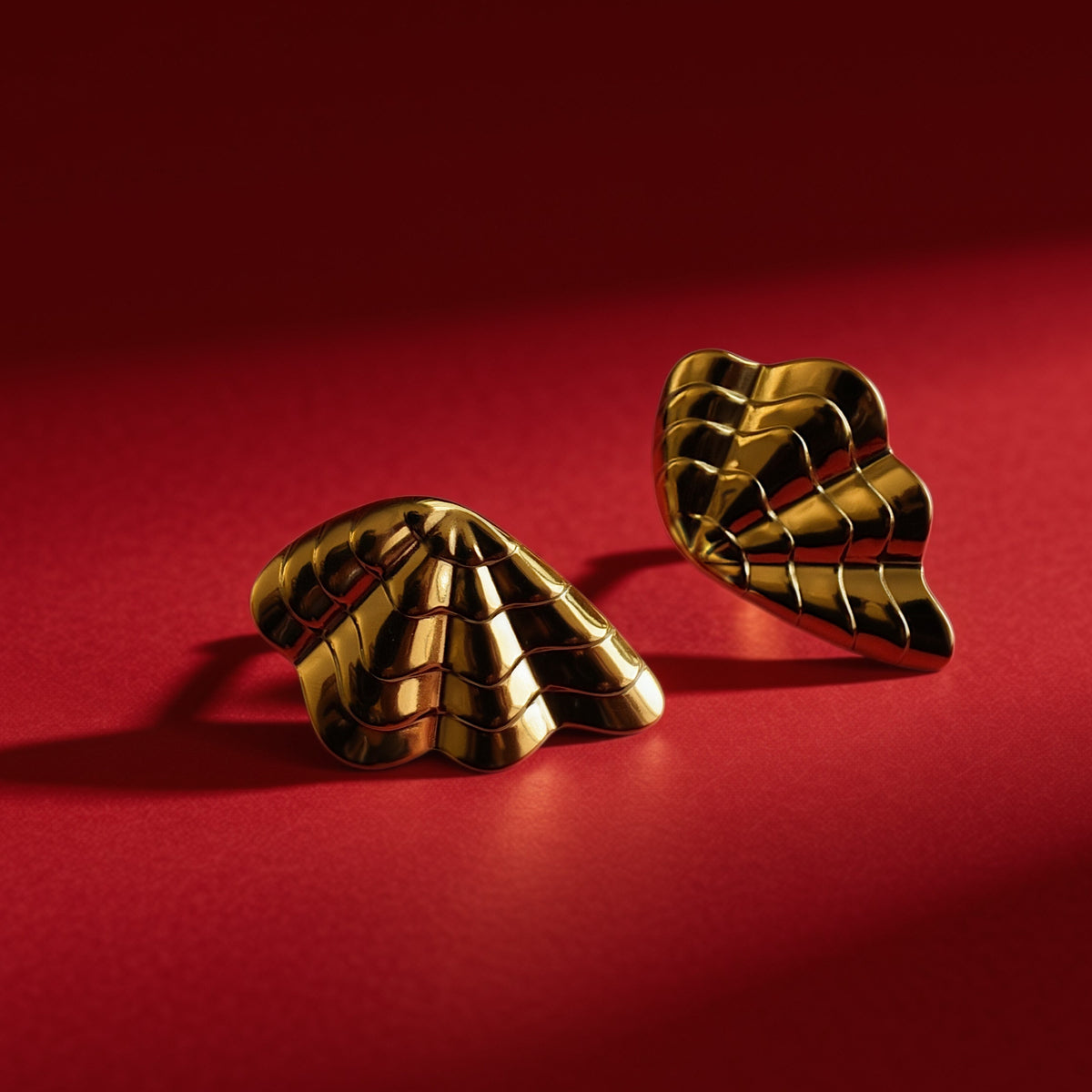 Gold shell earrings – angled view on red