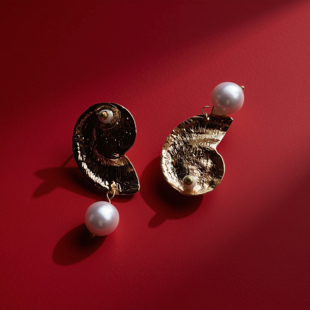 Schelp parel oorbellen goud – close-up op rood