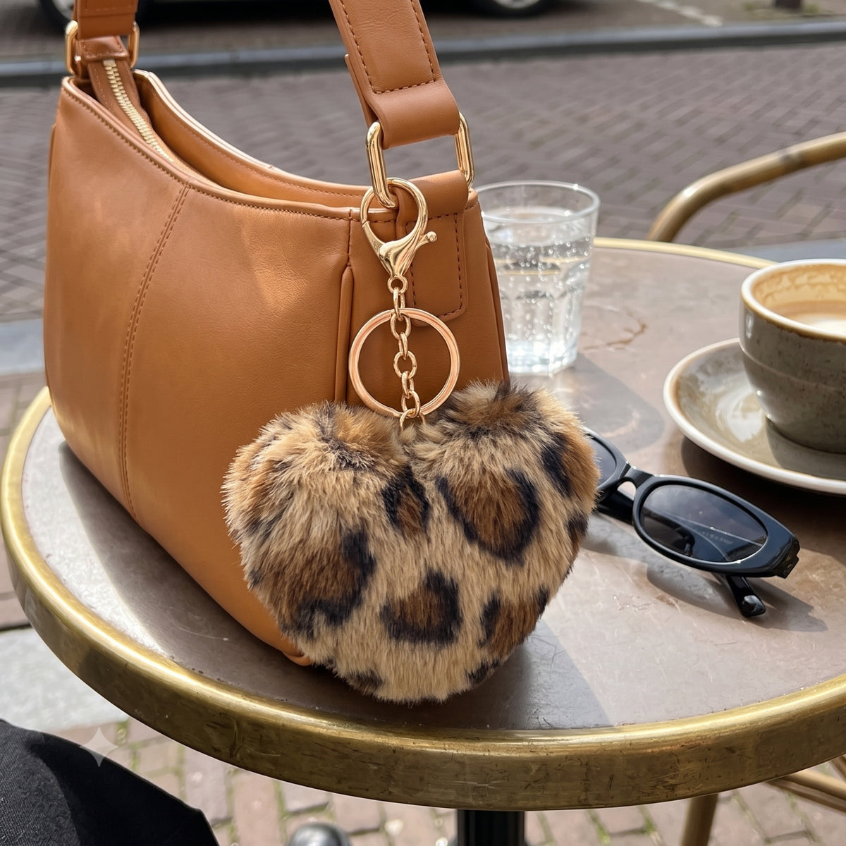 Fluffy hart bag charm met panterprint aan bruine tas bij terras